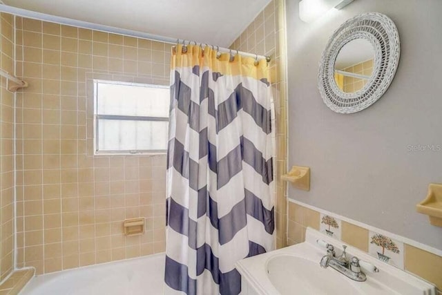 bathroom with shower / bath combo with shower curtain, sink, and tile walls