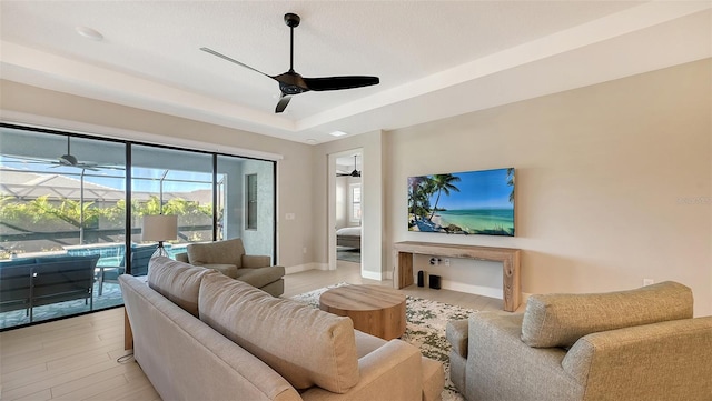 living room with ceiling fan, light hardwood / wood-style floors, and a tray ceiling