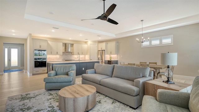 living room with a raised ceiling, light hardwood / wood-style flooring, ceiling fan with notable chandelier, and sink