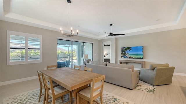 dining space with ceiling fan with notable chandelier, a raised ceiling, and light hardwood / wood-style flooring