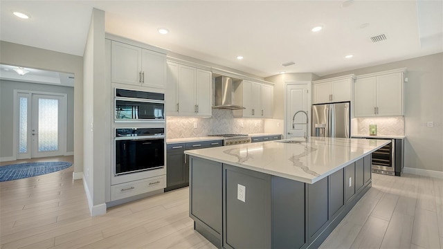 kitchen featuring white cabinetry, sink, wall chimney exhaust hood, an island with sink, and appliances with stainless steel finishes