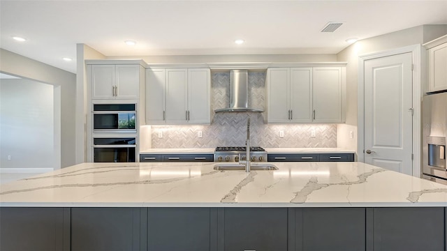 kitchen with stainless steel appliances, light stone countertops, wall chimney exhaust hood, and a spacious island