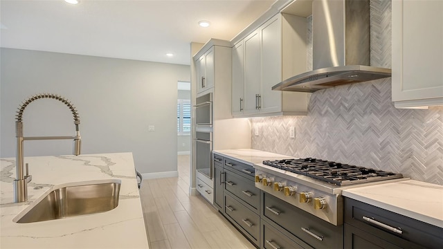 kitchen featuring light stone countertops, stainless steel appliances, sink, wall chimney range hood, and white cabinets