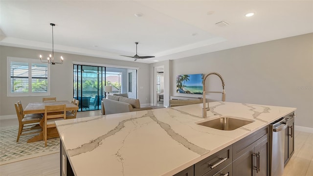 kitchen featuring light stone counters, sink, hanging light fixtures, and an island with sink