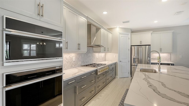 kitchen with light stone counters, wall chimney exhaust hood, stainless steel appliances, sink, and white cabinets