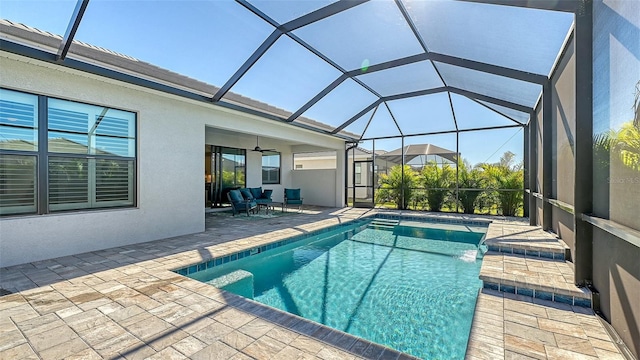 view of pool with outdoor lounge area, glass enclosure, ceiling fan, and a patio area