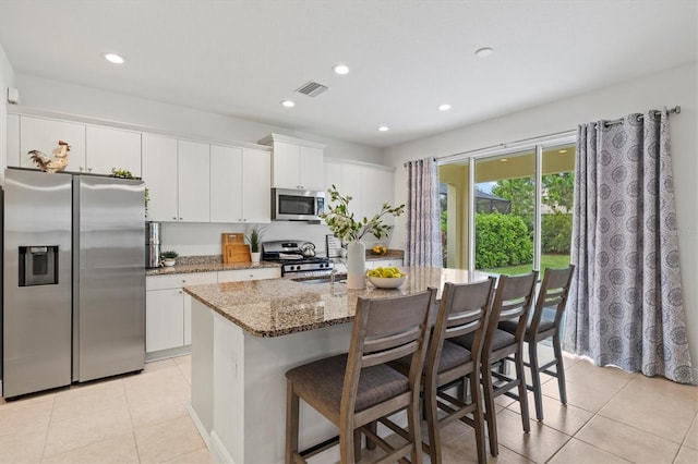 kitchen with white cabinetry, an island with sink, stone countertops, and appliances with stainless steel finishes