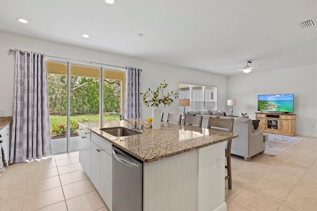 kitchen with dishwasher, white cabinets, a center island with sink, ceiling fan, and light stone counters