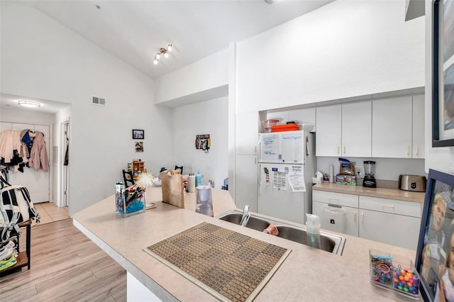 kitchen featuring white refrigerator, light hardwood / wood-style floors, sink, and high vaulted ceiling