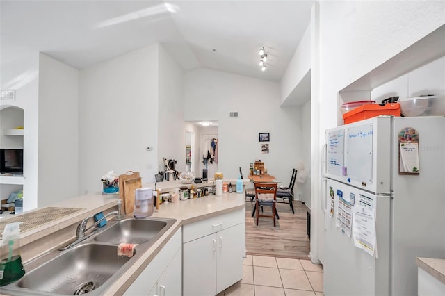 kitchen with sink, light tile patterned floors, white refrigerator, white cabinets, and lofted ceiling