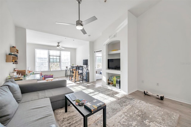 living room featuring ceiling fan, light wood-type flooring, and built in shelves