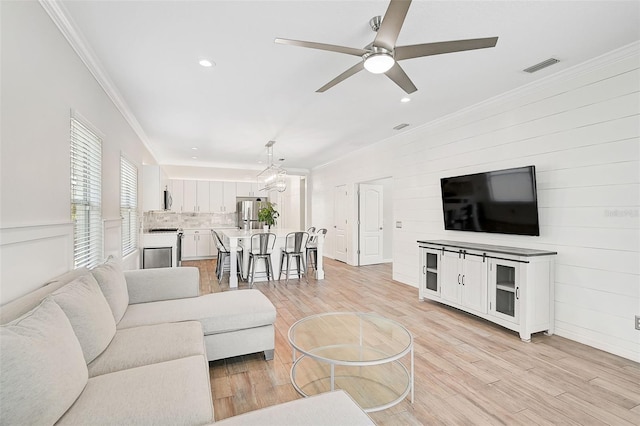 living room featuring ceiling fan with notable chandelier, light wood-type flooring, and ornamental molding