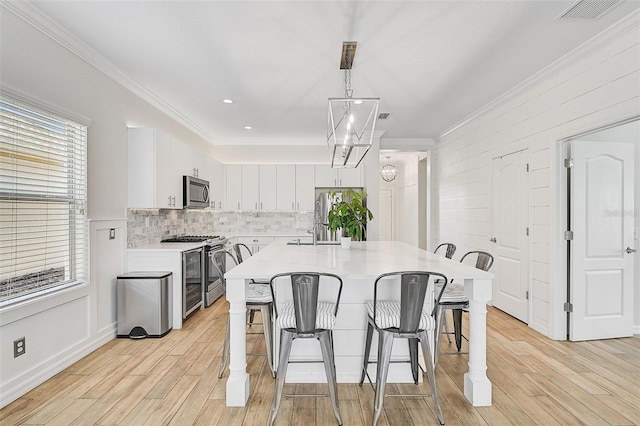 kitchen with pendant lighting, white cabinets, light hardwood / wood-style floors, and appliances with stainless steel finishes