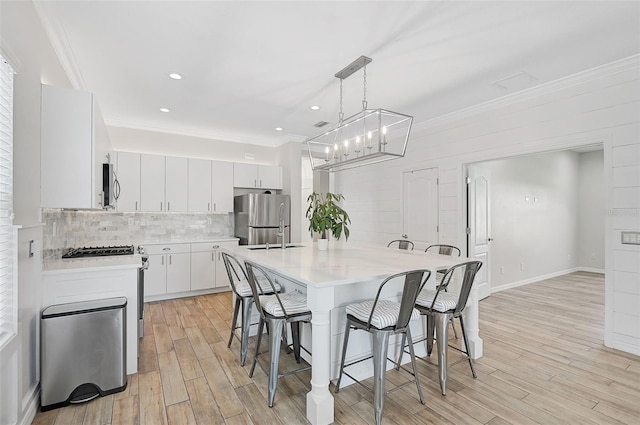 kitchen featuring appliances with stainless steel finishes, light hardwood / wood-style floors, white cabinetry, and decorative light fixtures