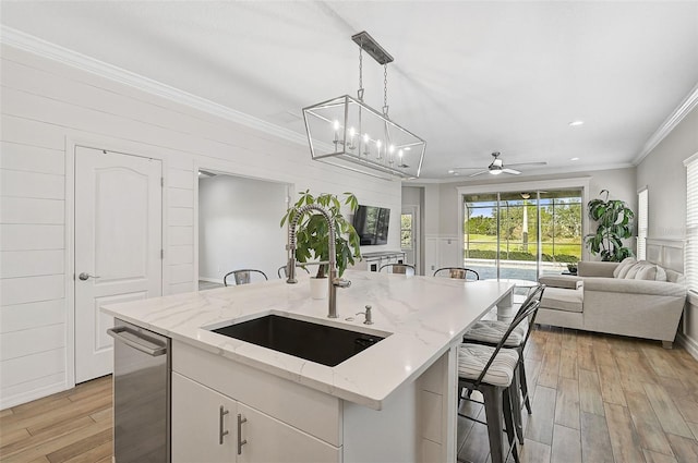 kitchen featuring sink, hanging light fixtures, stainless steel dishwasher, an island with sink, and white cabinetry