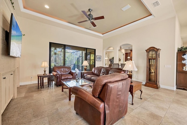 living room featuring a raised ceiling, ceiling fan, and ornamental molding