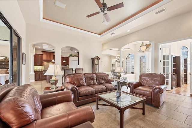 living room featuring a towering ceiling, ceiling fan with notable chandelier, a tray ceiling, and light hardwood / wood-style floors