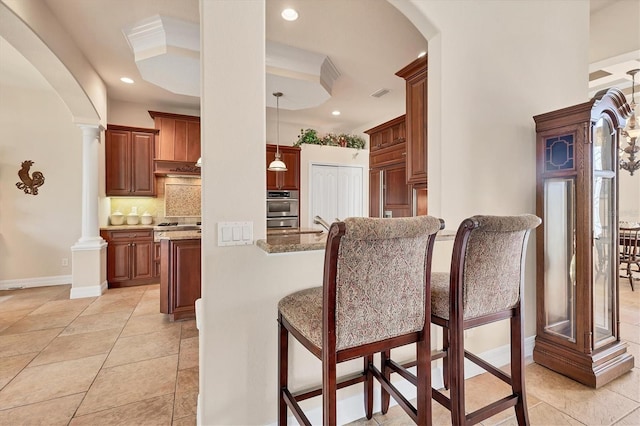 kitchen featuring tasteful backsplash, light stone counters, double oven, pendant lighting, and light tile patterned floors