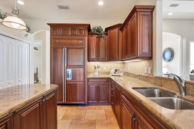 kitchen featuring tasteful backsplash, light stone counters, sink, pendant lighting, and paneled built in fridge