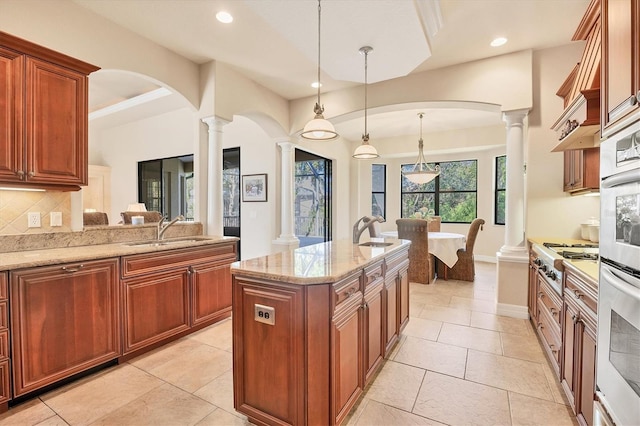 kitchen with pendant lighting, sink, decorative backsplash, light stone countertops, and appliances with stainless steel finishes