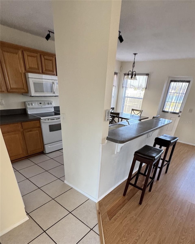 kitchen featuring an inviting chandelier, decorative light fixtures, white appliances, a breakfast bar, and light wood-type flooring