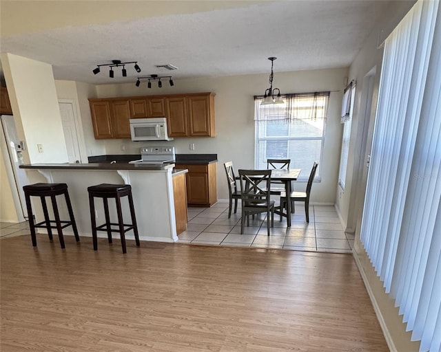 kitchen featuring pendant lighting, white appliances, light hardwood / wood-style floors, kitchen peninsula, and a breakfast bar area