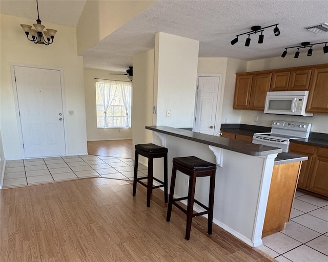 kitchen featuring light hardwood / wood-style flooring, decorative light fixtures, white appliances, a kitchen bar, and ceiling fan with notable chandelier