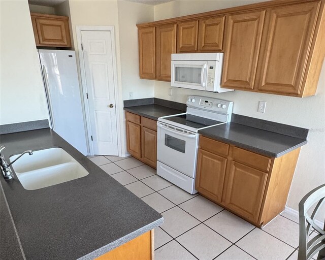 4042 Kingsfield Dr, Parrish, FL 34219 - kitchen with white appliances, dark countertops, a sink, light tile patterned flooring, and brown cabinetry