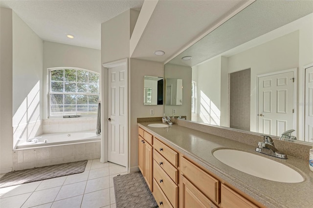 bathroom with a textured ceiling, vanity, tiled bath, and tile patterned floors