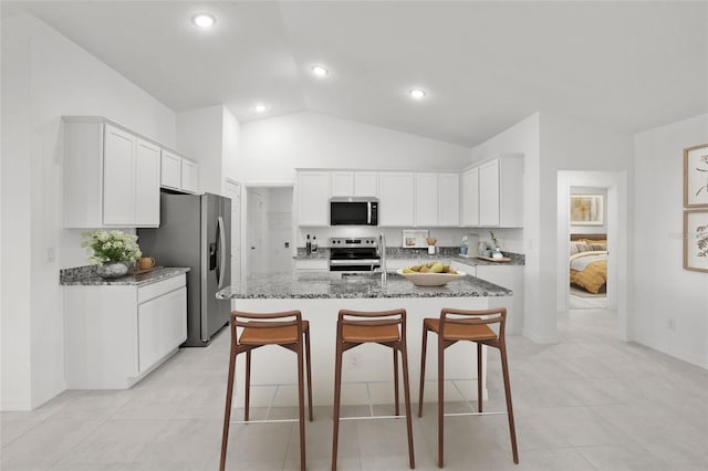 kitchen with appliances with stainless steel finishes, vaulted ceiling, stone countertops, white cabinets, and an island with sink