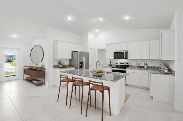 kitchen featuring appliances with stainless steel finishes, high vaulted ceiling, stone counters, white cabinets, and an island with sink