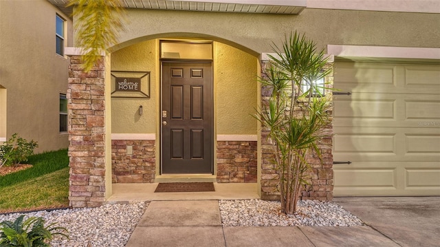 doorway to property featuring a garage, stone siding, concrete driveway, and stucco siding