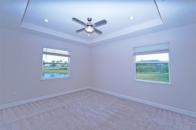 carpeted empty room featuring a tray ceiling, ceiling fan, and a water view