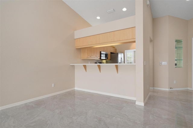 kitchen featuring light brown cabinets, a kitchen breakfast bar, high vaulted ceiling, kitchen peninsula, and appliances with stainless steel finishes