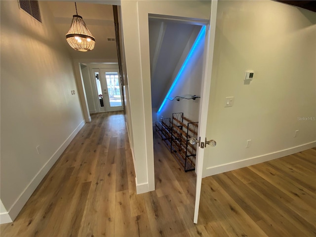 corridor featuring wood-type flooring and an inviting chandelier