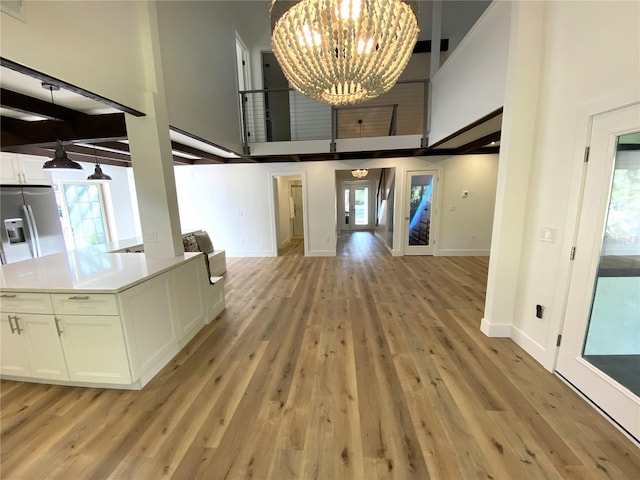 foyer entrance with beam ceiling, light hardwood / wood-style flooring, a towering ceiling, and a notable chandelier