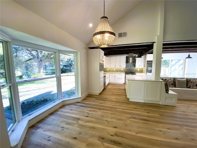 kitchen featuring white cabinetry, hanging light fixtures, wall chimney range hood, light wood-type flooring, and appliances with stainless steel finishes