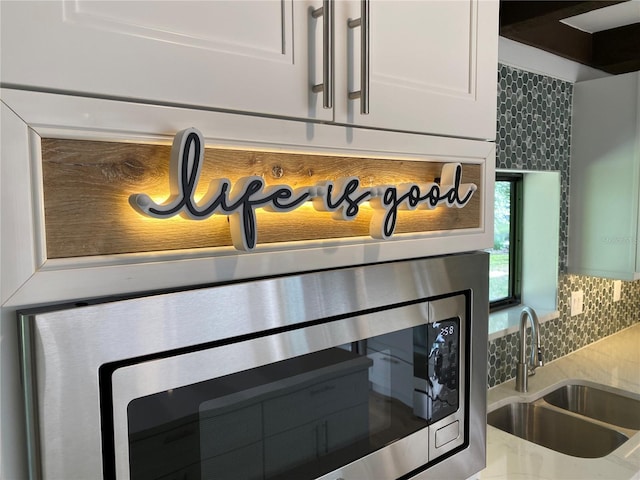 interior details with tasteful backsplash, white cabinetry, and sink