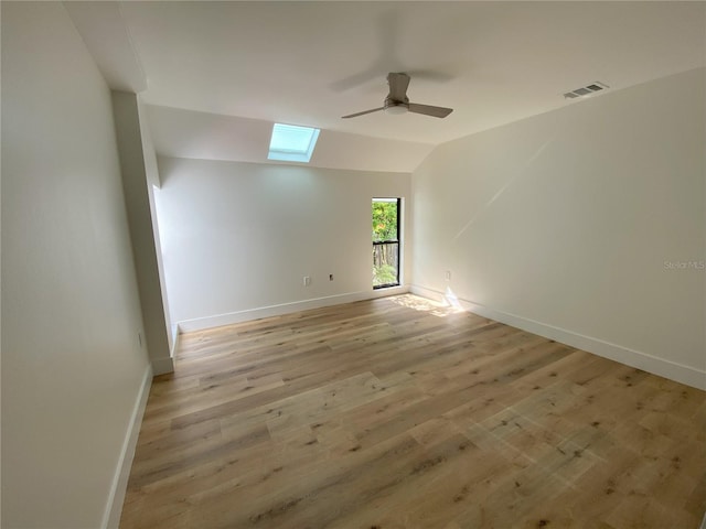 spare room featuring light wood-type flooring, ceiling fan, and vaulted ceiling with skylight