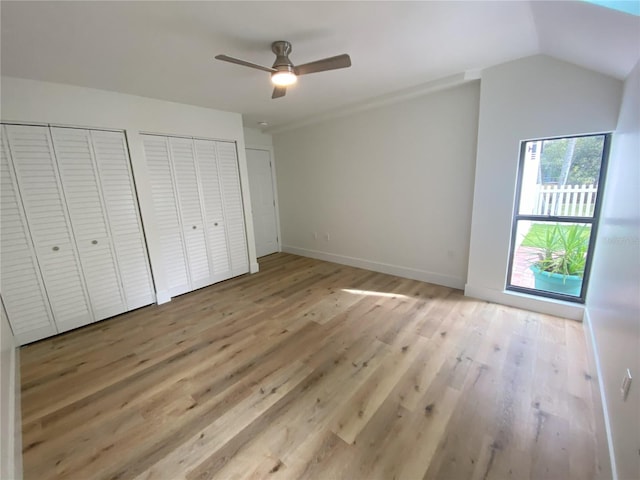 unfurnished bedroom featuring ceiling fan, light hardwood / wood-style floors, vaulted ceiling, and two closets