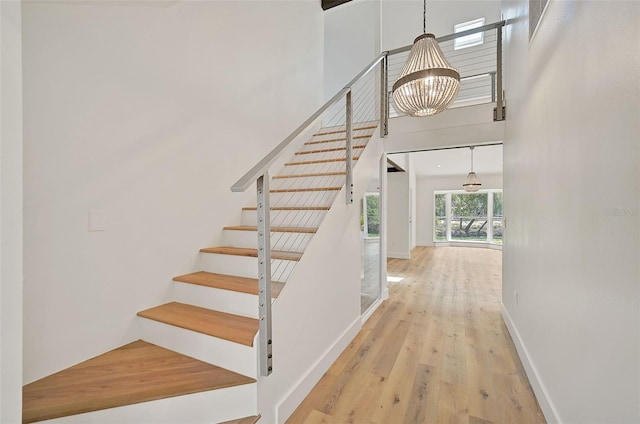 stairs with hardwood / wood-style flooring, a towering ceiling, and a notable chandelier