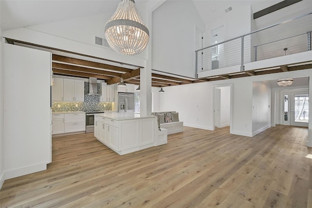 kitchen featuring a towering ceiling, stainless steel appliances, a notable chandelier, white cabinets, and wall chimney exhaust hood