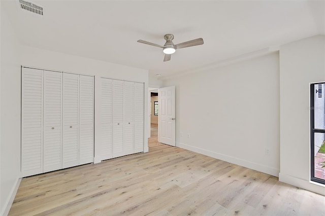 unfurnished bedroom with ceiling fan, light hardwood / wood-style flooring, and two closets