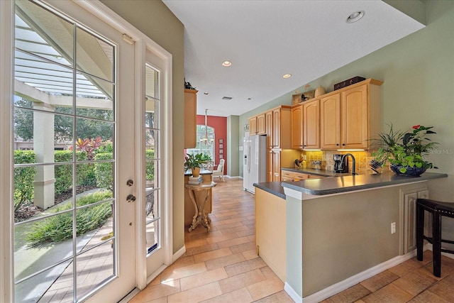 kitchen featuring white refrigerator with ice dispenser, hanging light fixtures, decorative backsplash, light brown cabinetry, and kitchen peninsula