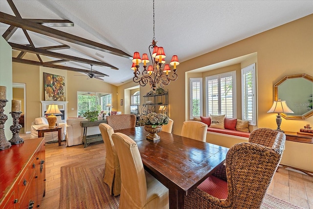 dining room with light wood-type flooring, a textured ceiling, lofted ceiling with beams, and ceiling fan with notable chandelier