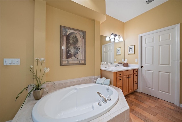 bathroom with vanity, a relaxing tiled tub, and wood-type flooring