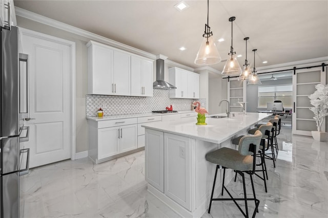 kitchen featuring pendant lighting, a center island with sink, white cabinets, wall chimney exhaust hood, and a barn door