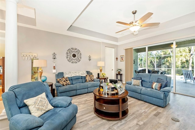 living room with light wood-type flooring, a raised ceiling, and ceiling fan