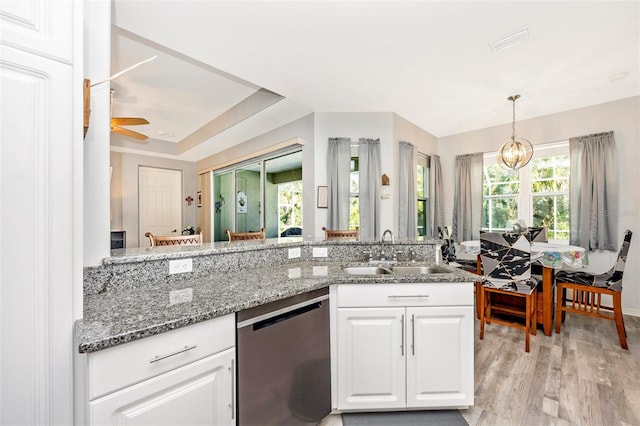 kitchen with stainless steel dishwasher, sink, dark stone countertops, white cabinets, and light hardwood / wood-style floors