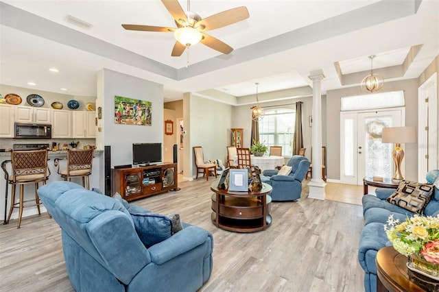 living room with ceiling fan with notable chandelier, a tray ceiling, and light hardwood / wood-style flooring